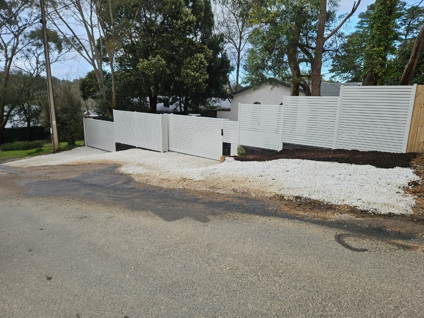 White aluminium slat sliding gate and fence on a gravel driveway