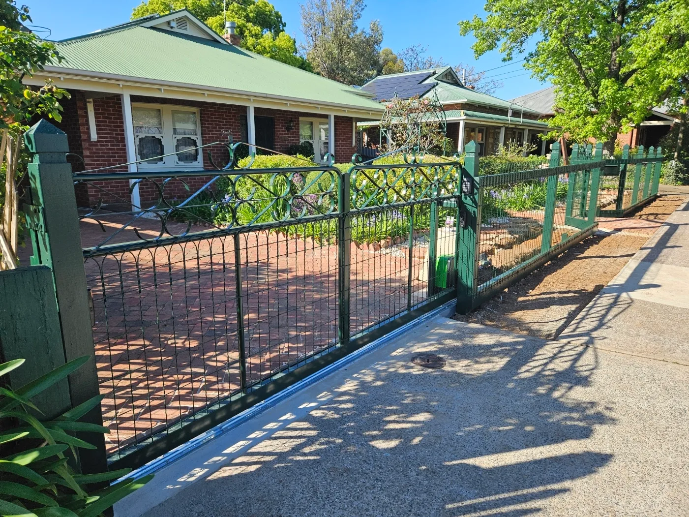 Green steel swing gates across a brick-paved driveway