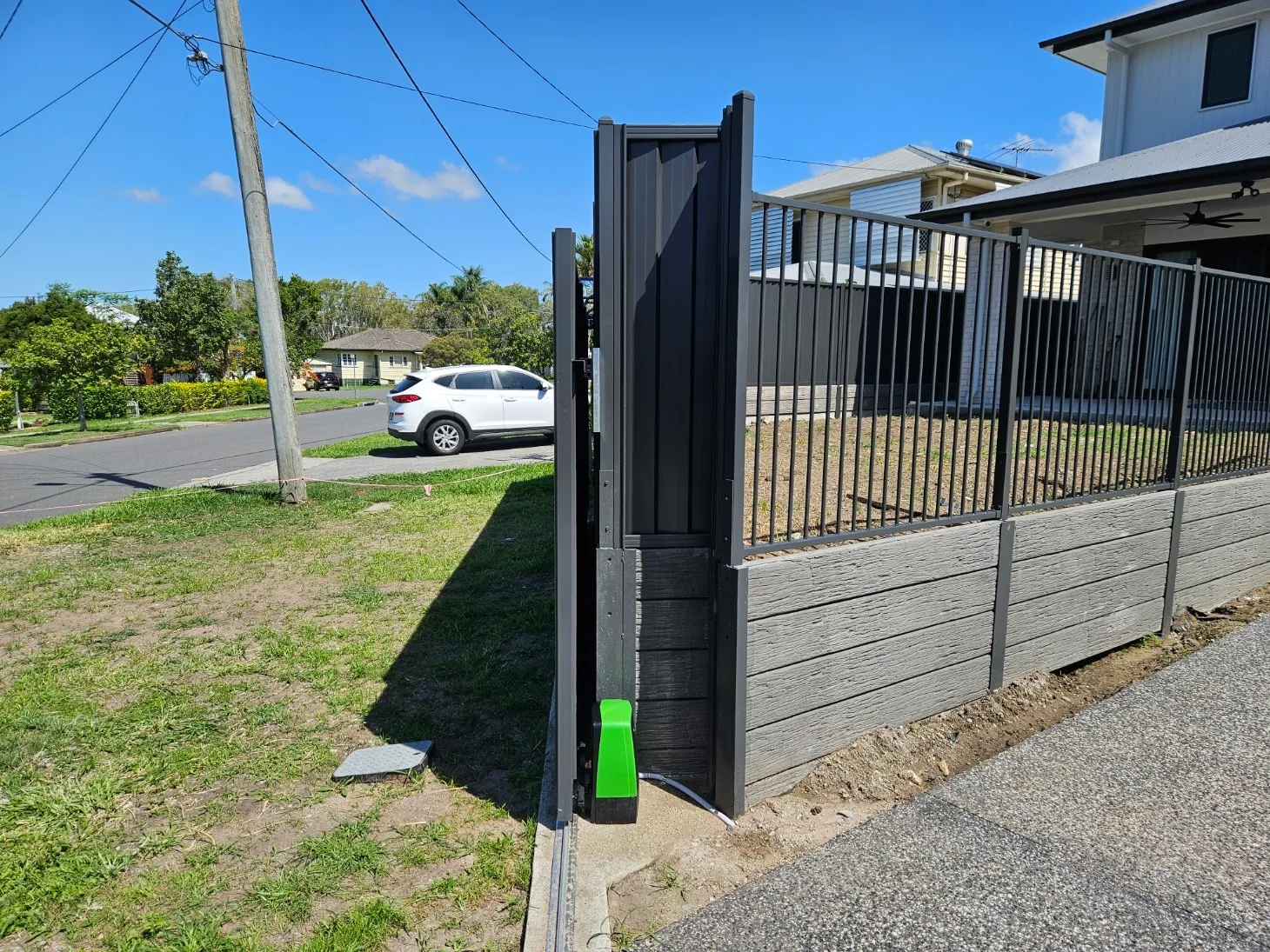 Black slat gate and fence with a gate motor post beside the footpath