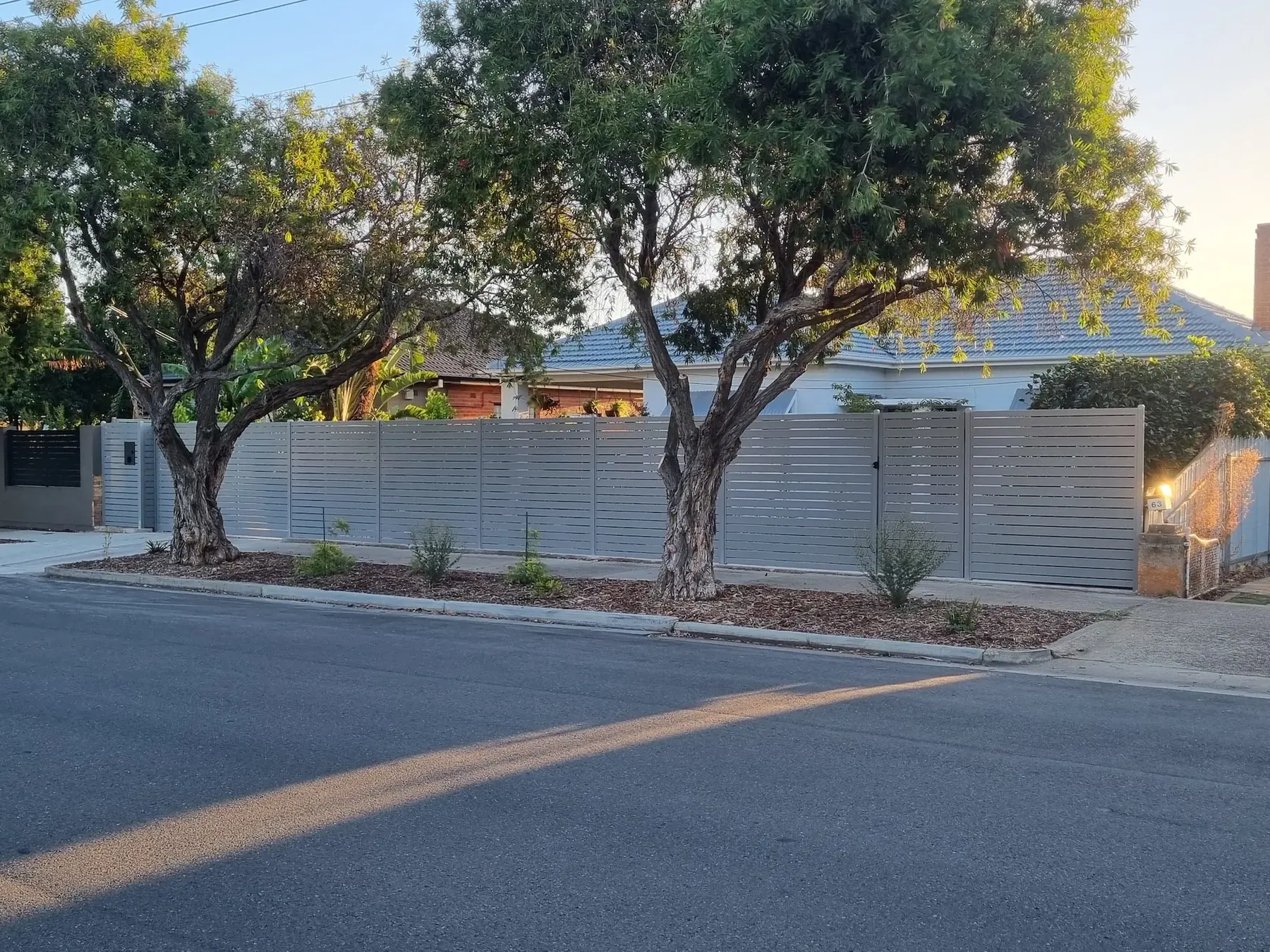 Grey aluminium slat front fence and driveway gate under gum trees