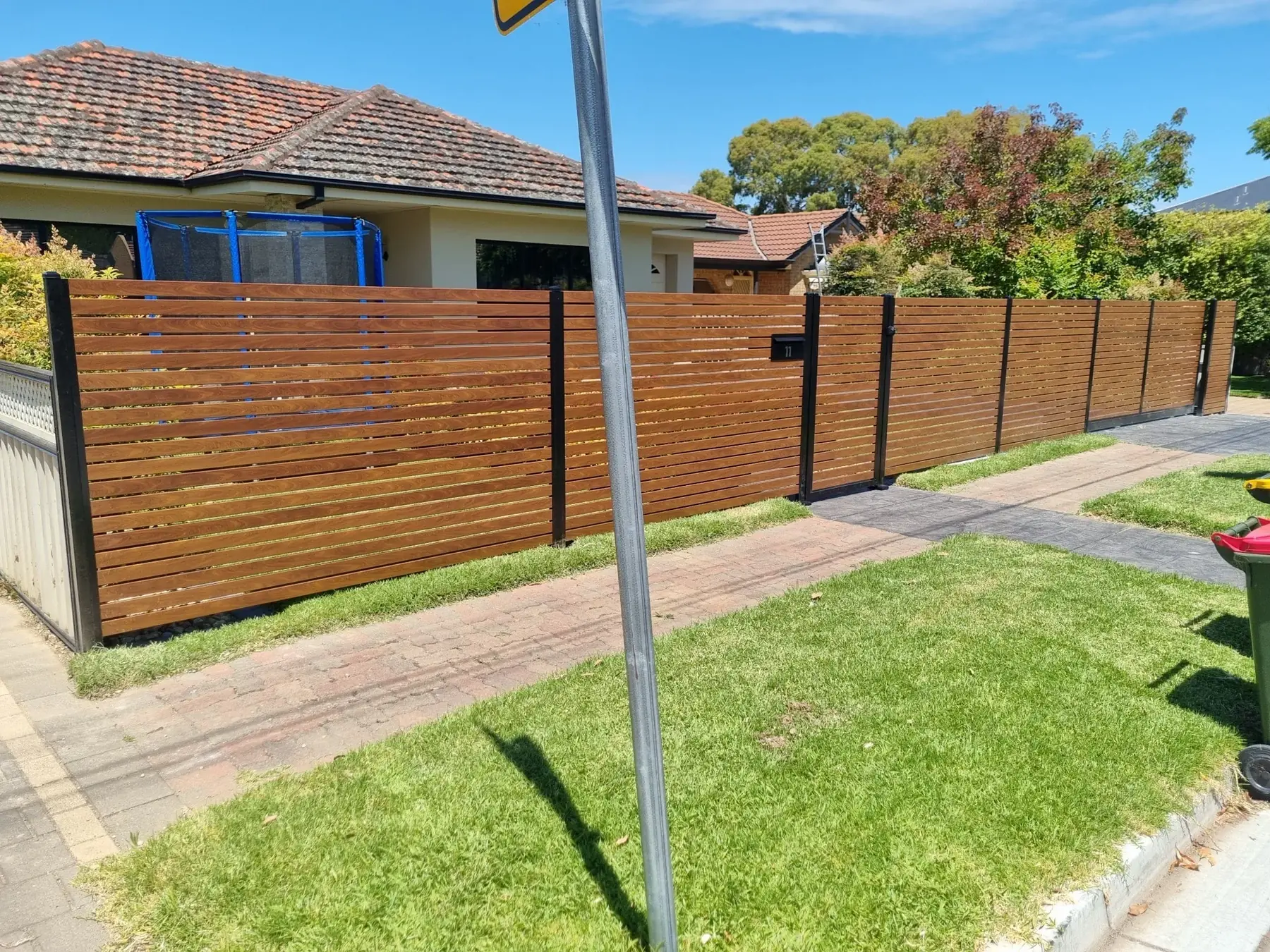 Timber-look aluminium slat gate and fence along a footpath